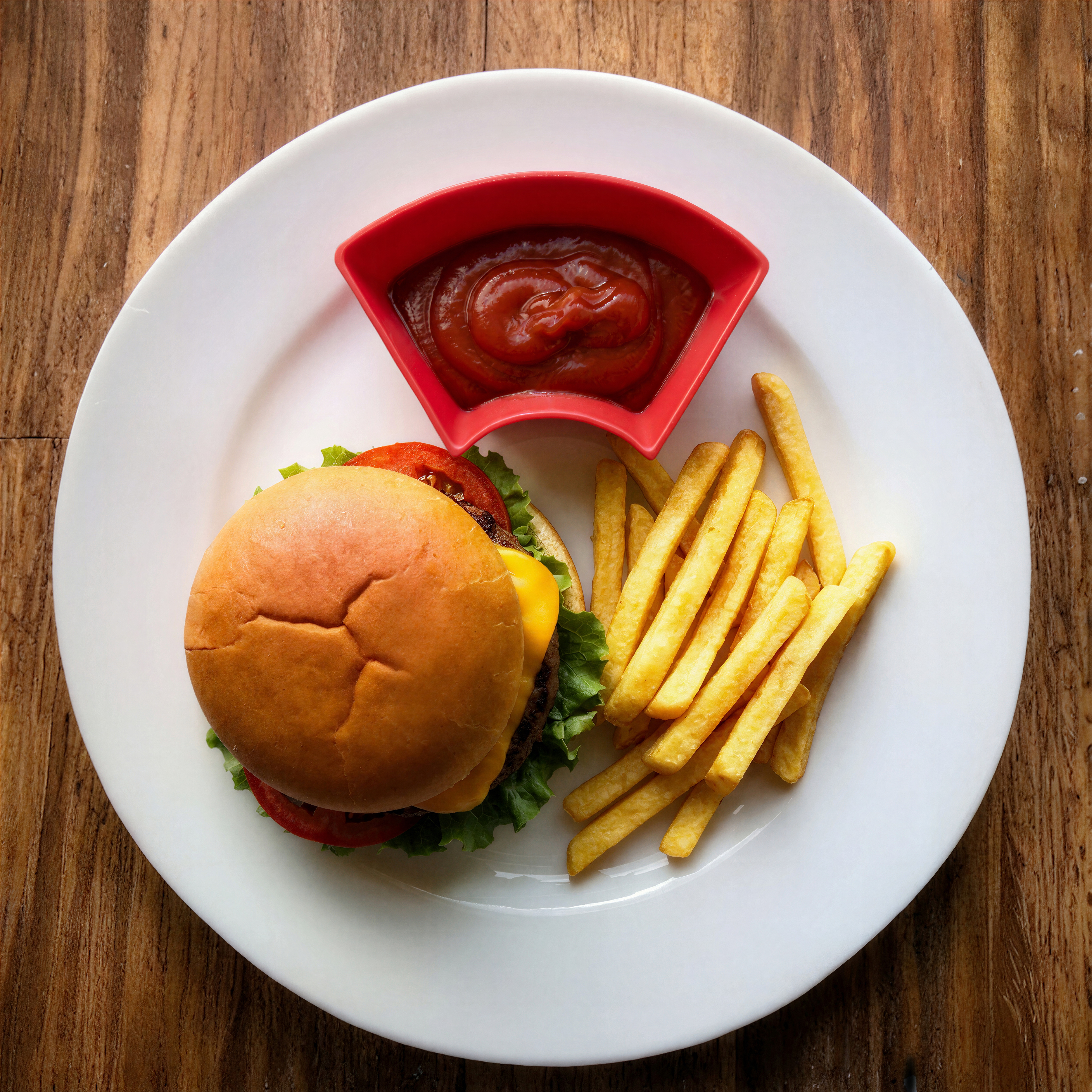 A red Diptrough full of ketchup on a plate beside a burger and fries